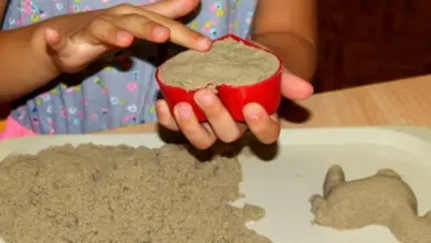 Dítě drží červenou nádobu s polymerním pískem nad podnosem.