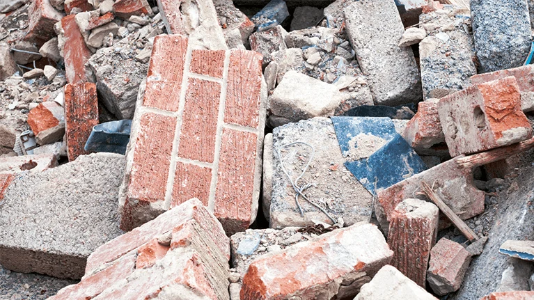 Hromada rozbitých cihel a betonu vyvolávající prach při demolici.