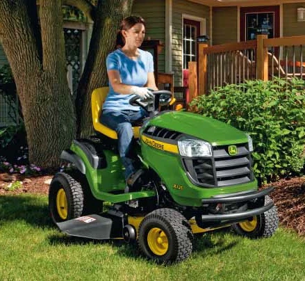 Žena řídí zelený traktor John Deere na trávníku.