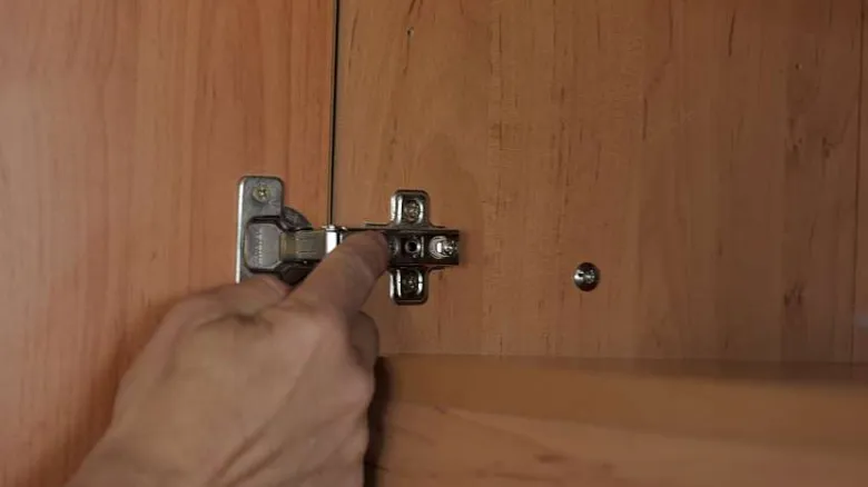 Ruka upravuje pant na dvířku kuchyňské skříňové linky.