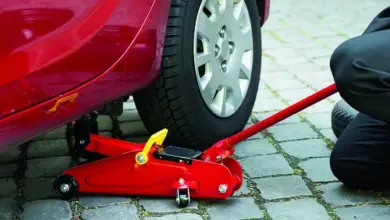 Červený hydraulický zvedák podzdvihuje červené auto na dlažbě.