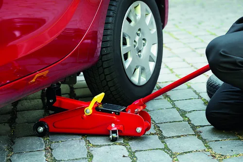 Červený hydraulický zvedák podzdvihuje červené auto na dlažbě.