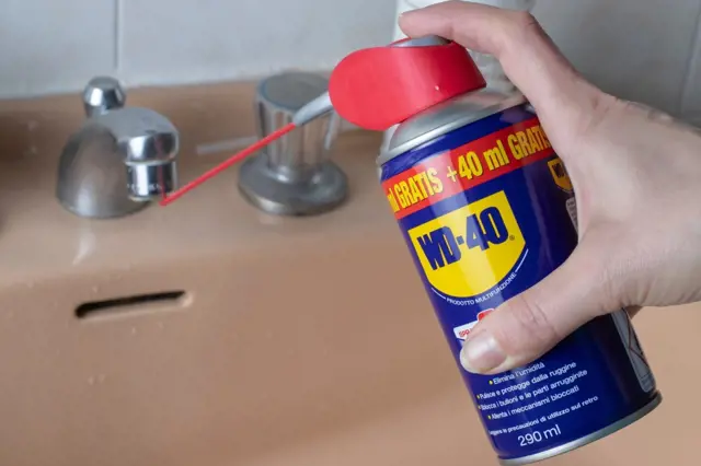 Ruka drží sprej WD-40 nad umyvadlem s kohoutkem.