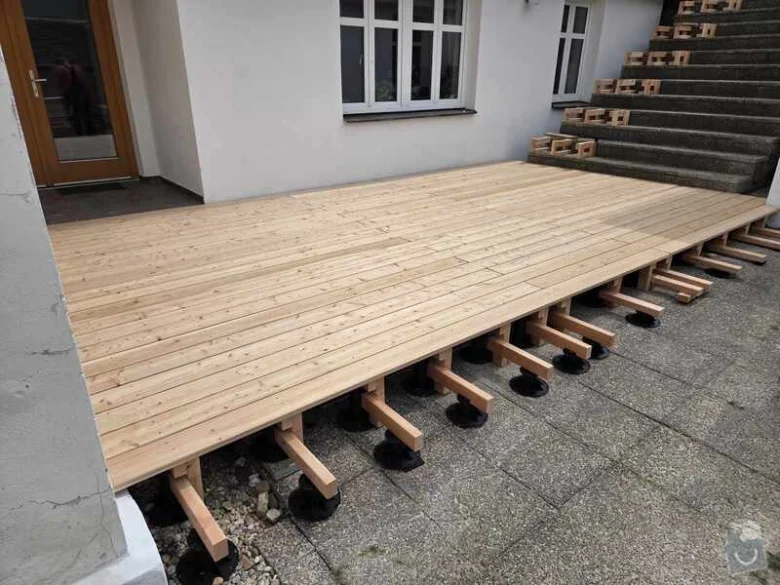 Nová dřevěná terasa z modřínu v procesu instalace s podložkami.