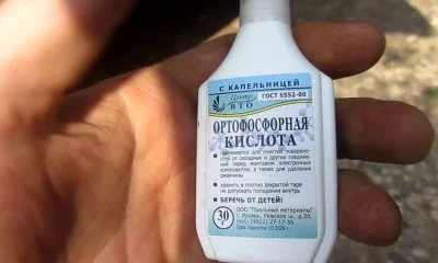 Ruka drží lahvičku ortofosforečné kyseliny s ruským nápisem.