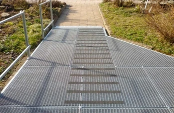 Venkovní přístupová rampa s kovovými roštmi pro invalidní vozíky.