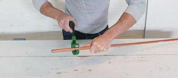 Muž řezí měděnou trubku pro výrobu antény.
