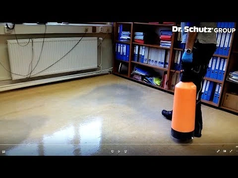 Osoba hladí podlahu z linolea bez vln pomocí spreje.