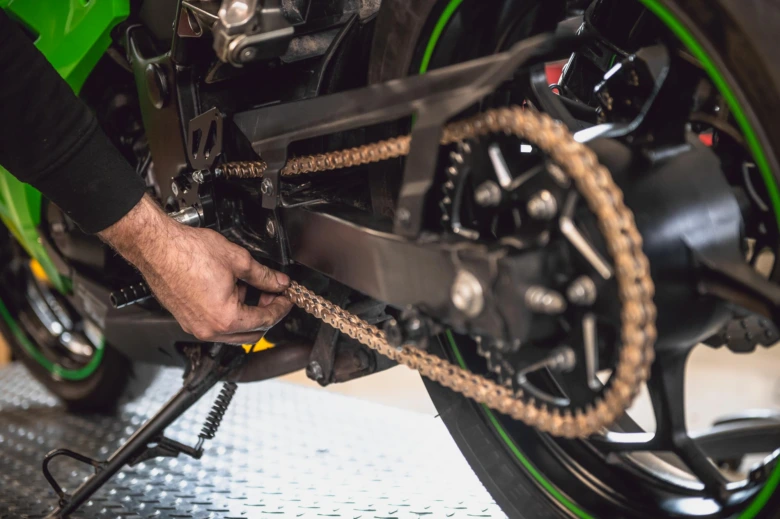 Ruka kontroluje napnutí řetězu na motocyklu pro správné nastavení.
