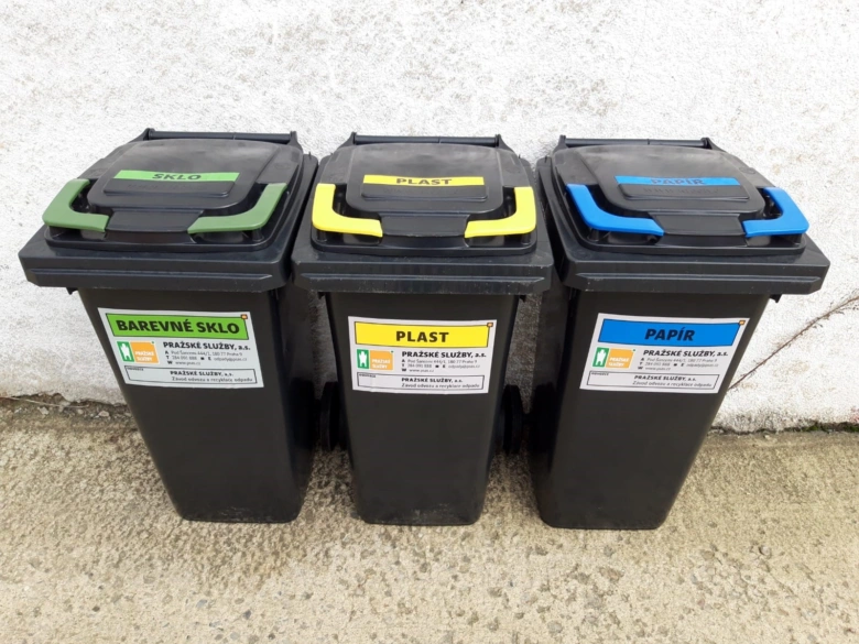 Tři kontejnery na recyklaci umístěné venku u domu.