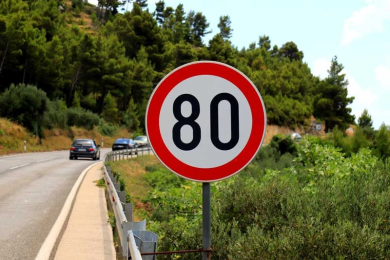 Rychlostní značka s limitem 80 km/h na silnici mezi stromy.