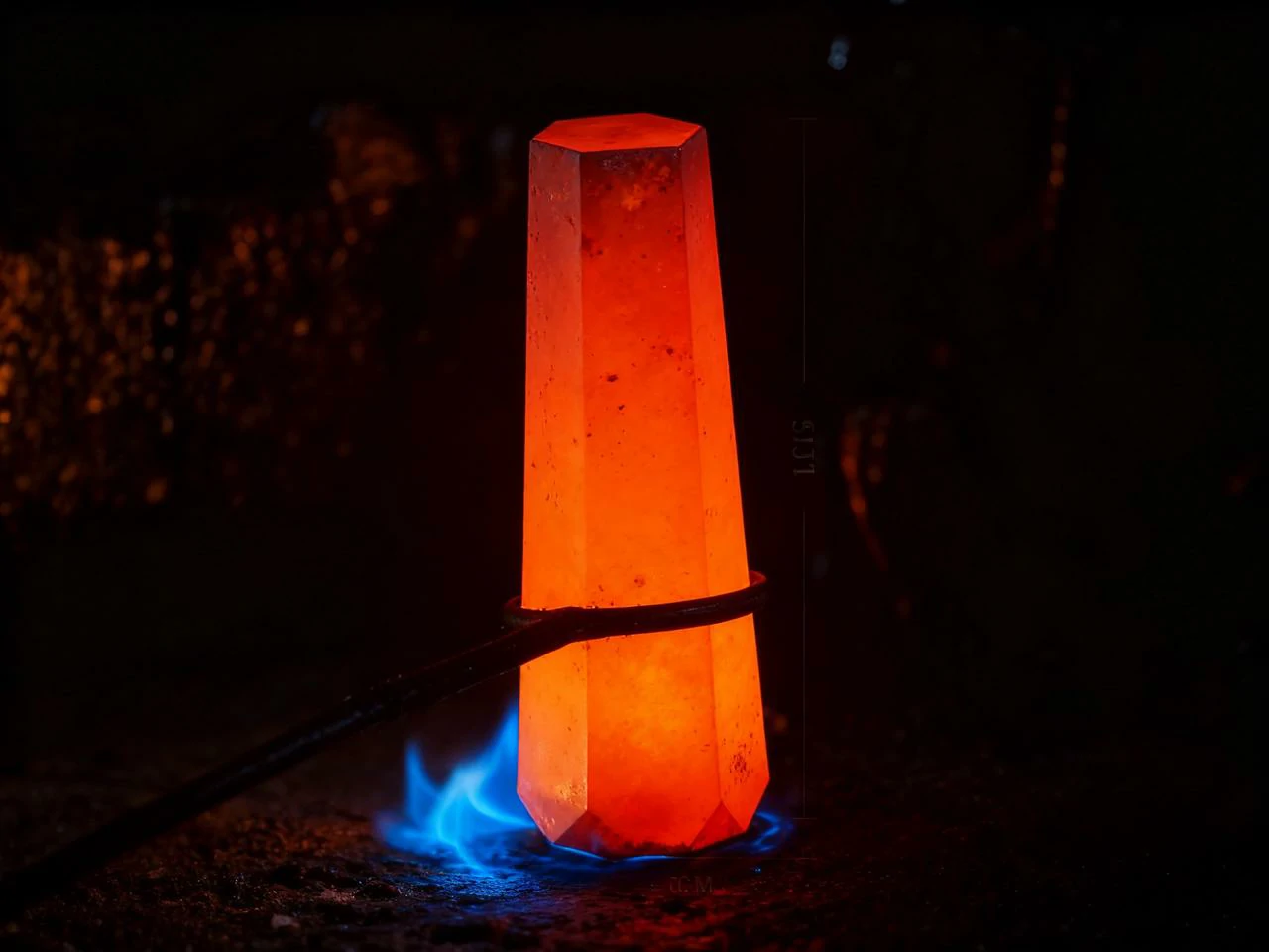 Horká ocelová prut držený nad plamenem při tepelném zpracování.