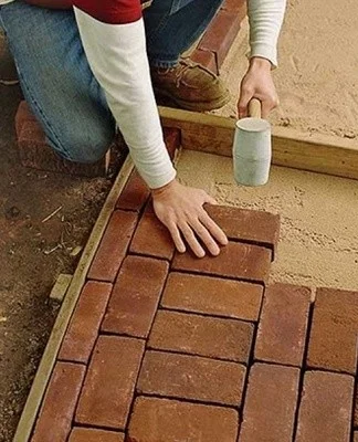 Muž kladne červené dlaždice na písek pro zahradní cestu.