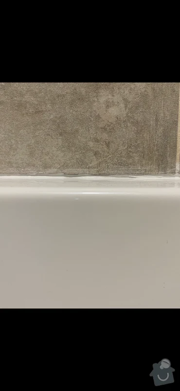 Mezera mezi bílou vanou a dlaždicovou stěnou.
