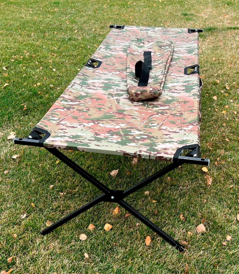 Kamuflovaná vojenská postel rozložena na trávníku.