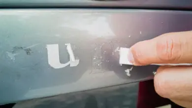 Ruční odstraňování lepidla z povrchu automobilu pomocí bílé podložky.