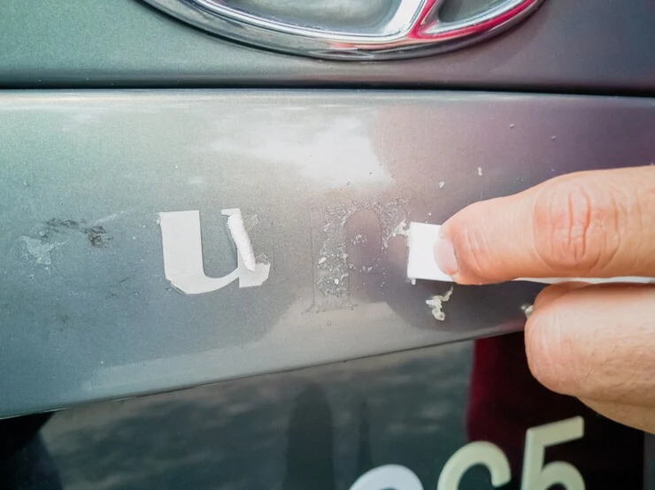 Ruční odstraňování lepidla z povrchu automobilu pomocí bílé podložky.