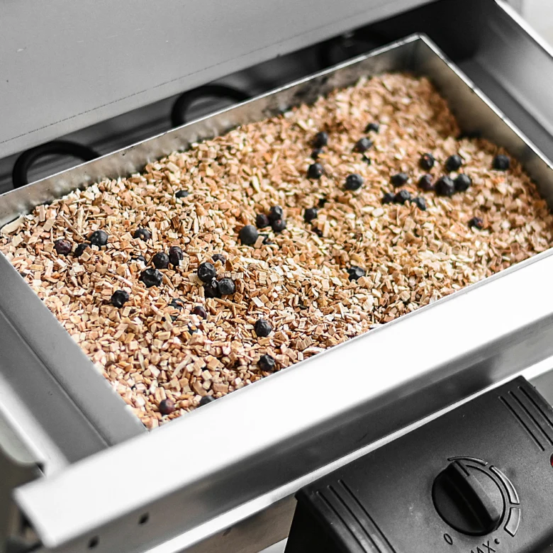 Tray s dřevěnými štěpkami a borůvkami v elektrickém kouřáku.