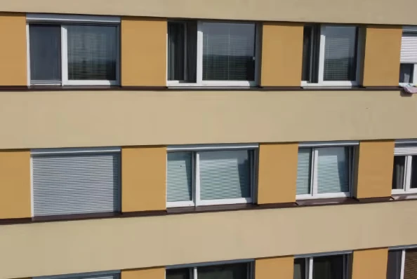Fotografie fasády bytového domu s okny na žluté zdi.