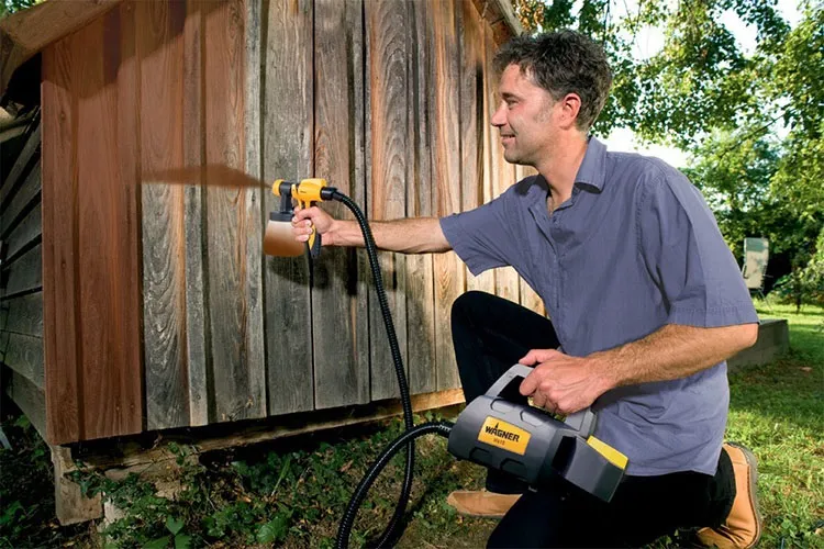 Muž stříká barvou na dřevěnou zeď pomocí elektrické pistole.