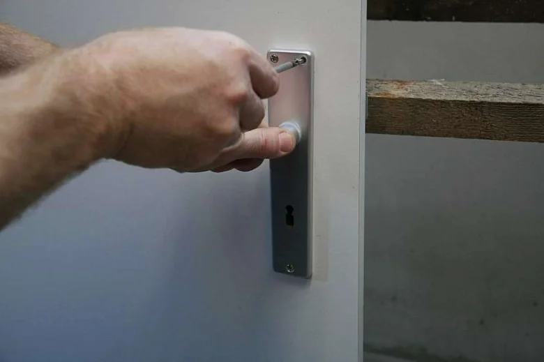 Ruka šroubuje kovovou desku zámku na bílou bránu.
