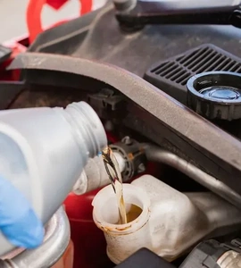 Nalévání hydraulického oleje do nádrže pod kapotou automobilu.