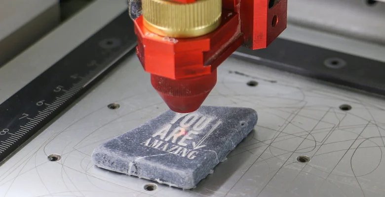 Laser gravíruje bílý nápis na šedém kamenném bloku.