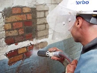 Pracovník čistí cihlovou zeď od malty a cementu pískováním.