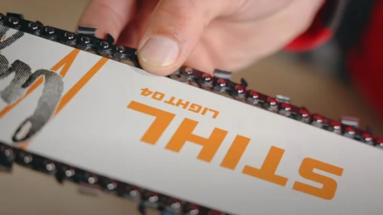 Ruka drží řetězovou pilu značky Stihl s vidlicí.