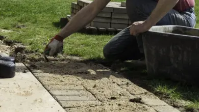 Muž klade dlaždice na písek pro zahradní cestu.