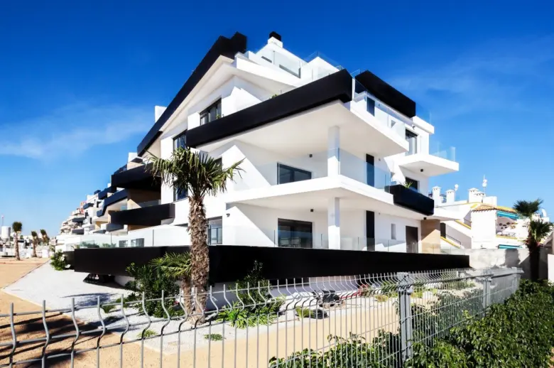 Moderní bílá budova s černými architektonickými prvky na pláži.