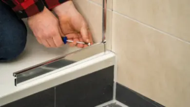Muž šroubuje kovový rám sprchových dveří