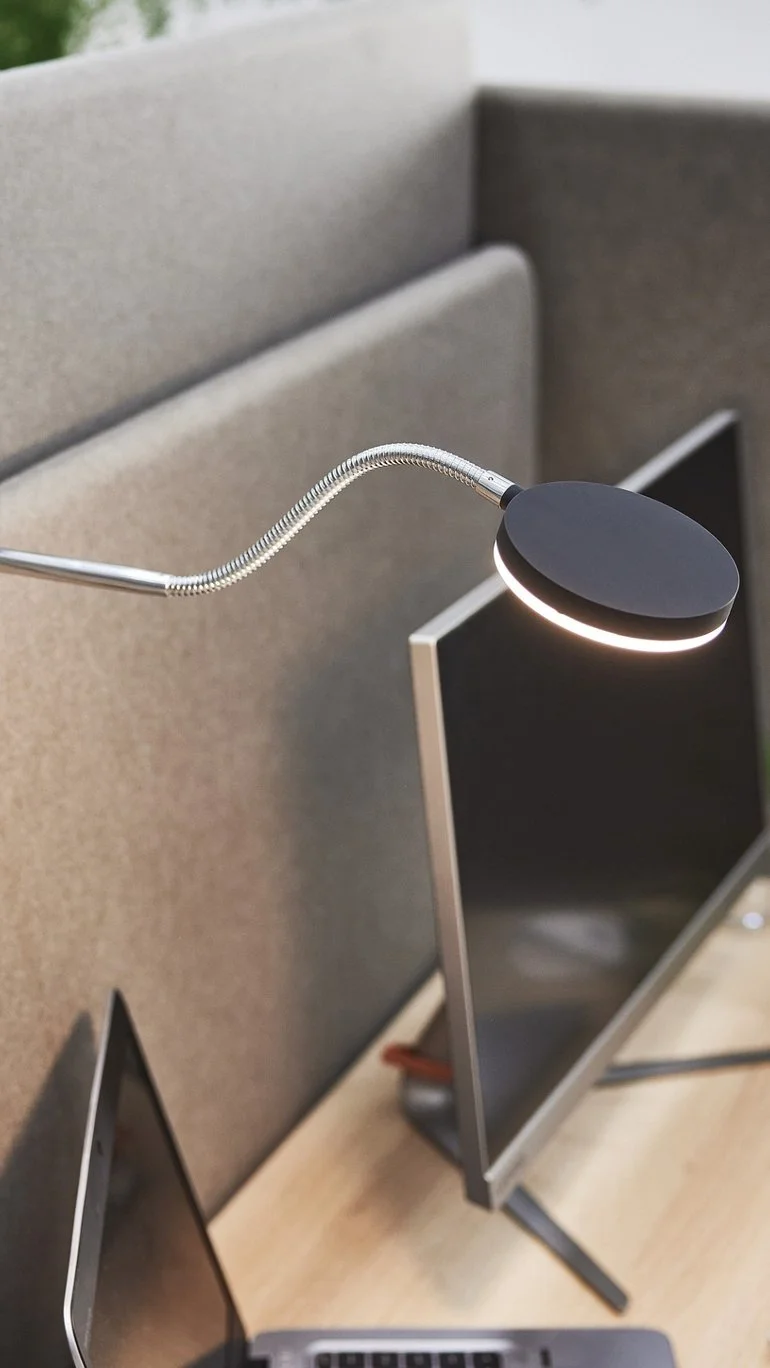 Moderní kancelářská lampa nad počítačem v ergonomickém pracovním prostoru.