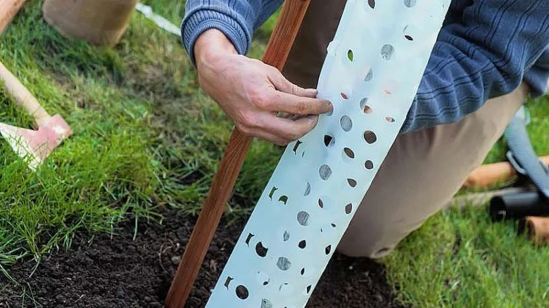 Osoba řezá větev stromu pomocí speciálního nůžku pro zahradní údržbu.