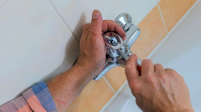 Ruční oprava kuchyňské baterie pomocí klíče na dlaždicovém pozadí.