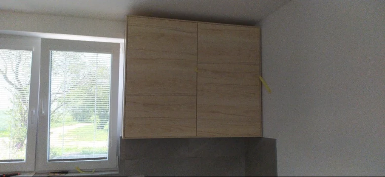 Nově nainstalovaná dřevěná kuchyňská skříň pod stropem s páskou.