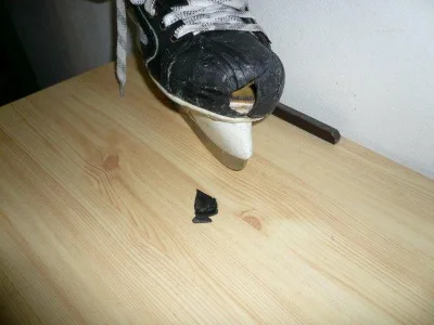 Poškozený plastový díl na kovovém čepele brusle ležící na dřevě.