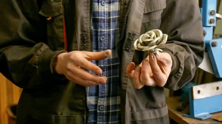 Dokončená železná růže držená v ruce člověka.