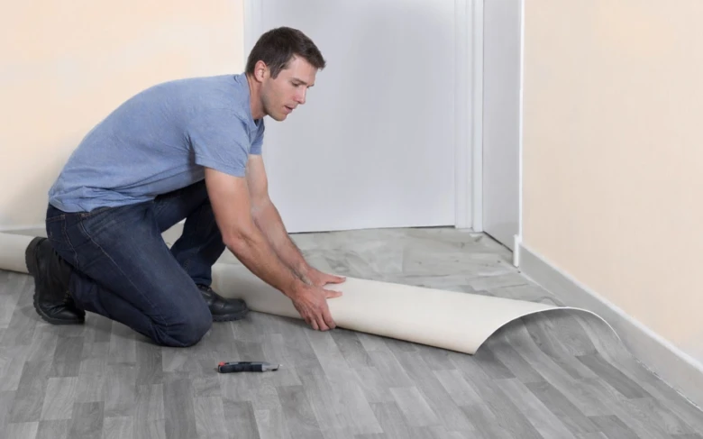 Muž leží na podlaze a roztahuje nové linoleum.