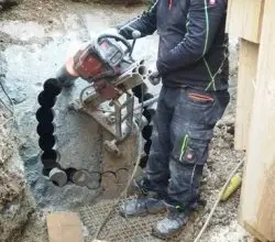 Pracovník vrtá beton velkým diamantovým vrtákem.