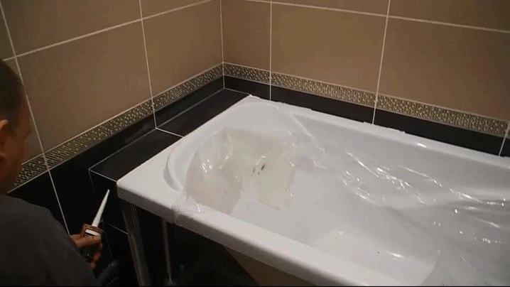 Muž aplikuje těsnicí hmotu do mezery mezi vanou a obložením.
