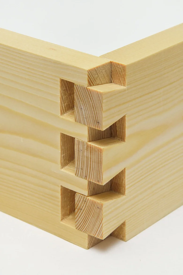 Detail dřevěného spojení v rohu pomocí klínových čtvercových hřebenů.