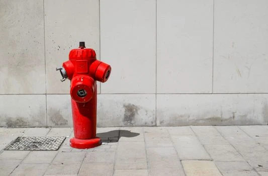 Červený požární hydrant na chodníku před bílou zdí.