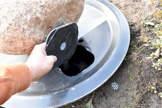 Ruka drží černou část fontány v kovovém podstavci.