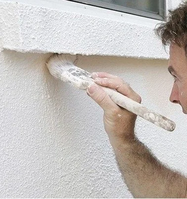 Muž nanáší fasádní omítку štětcem na zdi.