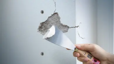 Ruce opravují trhlinu ve zdi špachtlí s hmotou před malováním.