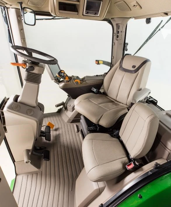 Vnitřek kabiny traktoru John Deere s sedadly a ovládacími prvky.