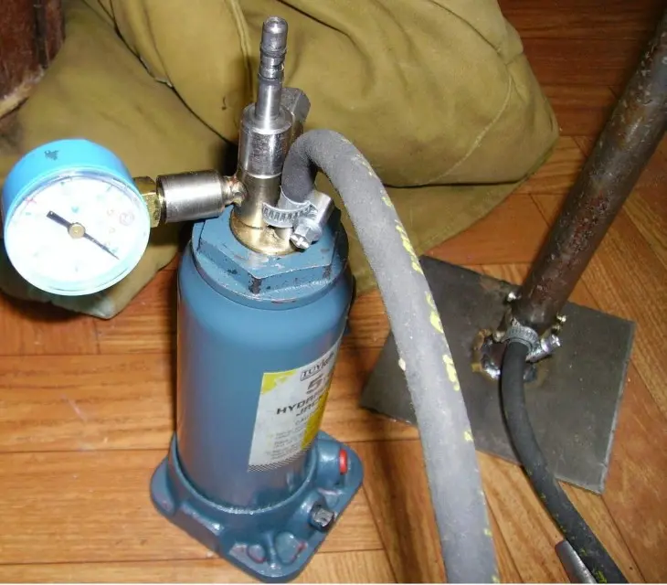 Modrá hydraulická čerpadlo s manometrem na dřevěné podlaze.