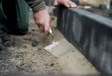 Ruka natířá maltu podél okraje zahradního oblouku.
