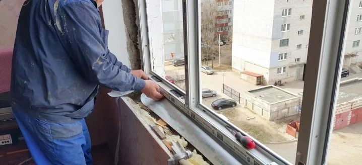 Muž opravuje plastové okno v bytě s použitím izolační pěny.